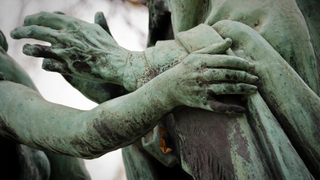 A bronze statue that has turned pale green with arms reaching towards each other.